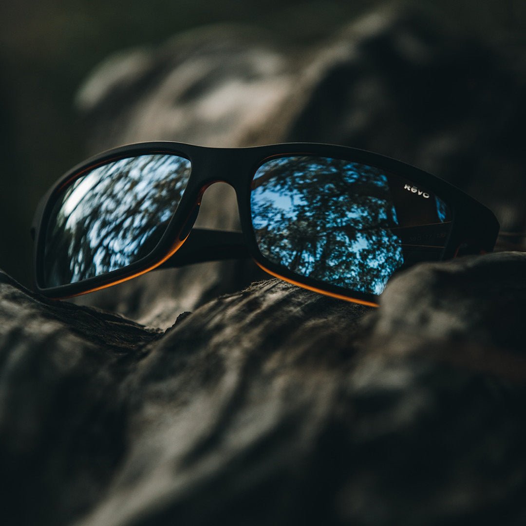 Sunglasses with reflective surface resting on rocks.