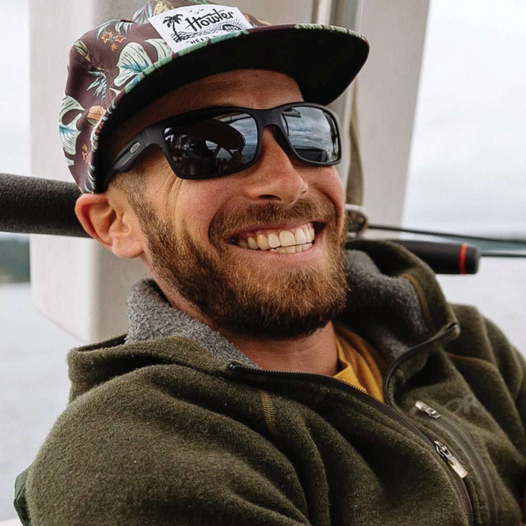 Man wearing sunglasses and a cap smiling outdoors.