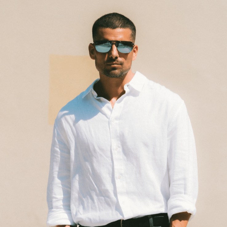 Man wearing a white shirt and sunglasses against a beige wall