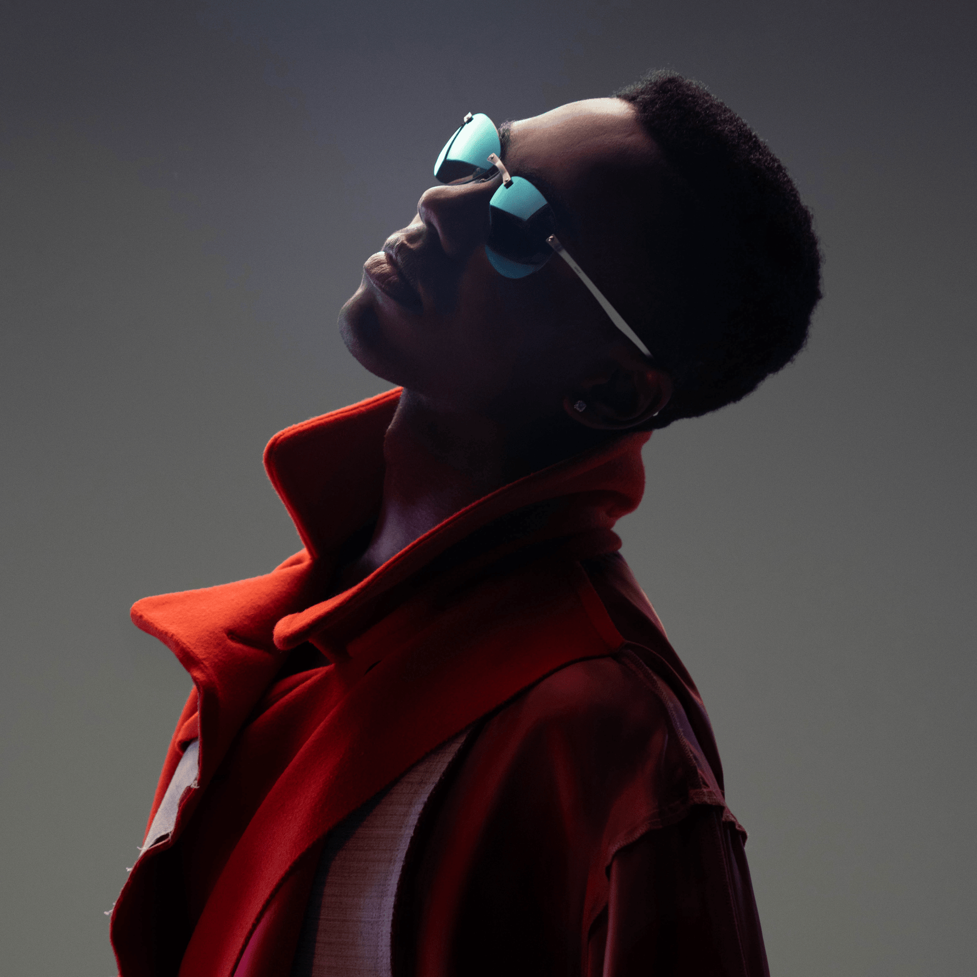 Person wearing a red coat and sunglasses against a dark background