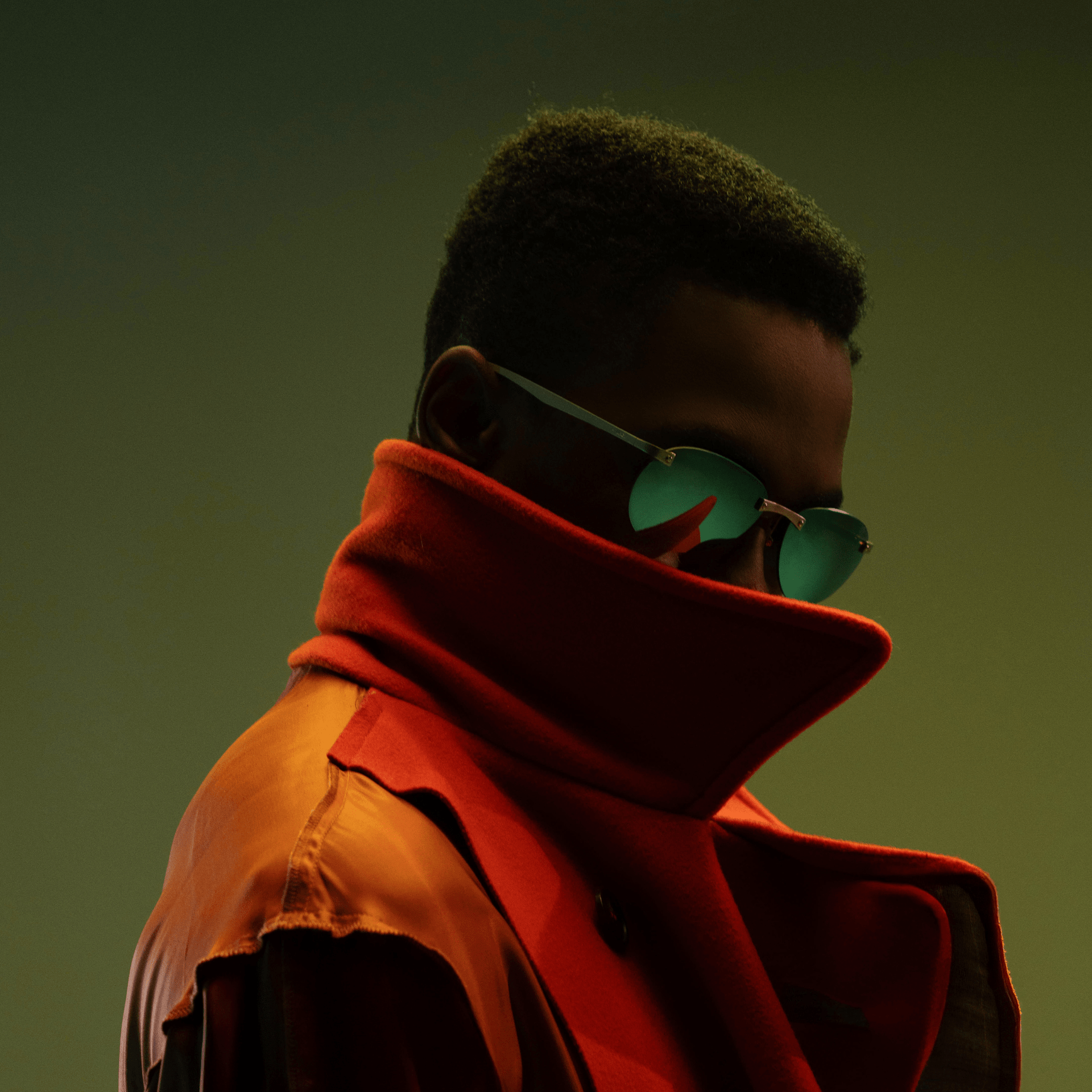 Person wearing a red coat and green sunglasses against a dark background