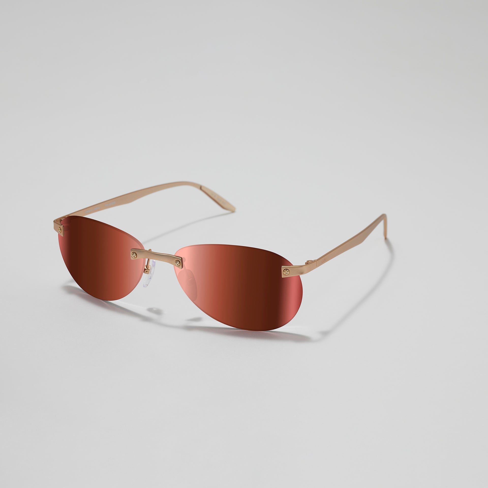 Sunglasses with gold frame and red-tinted lenses on a light gray background
