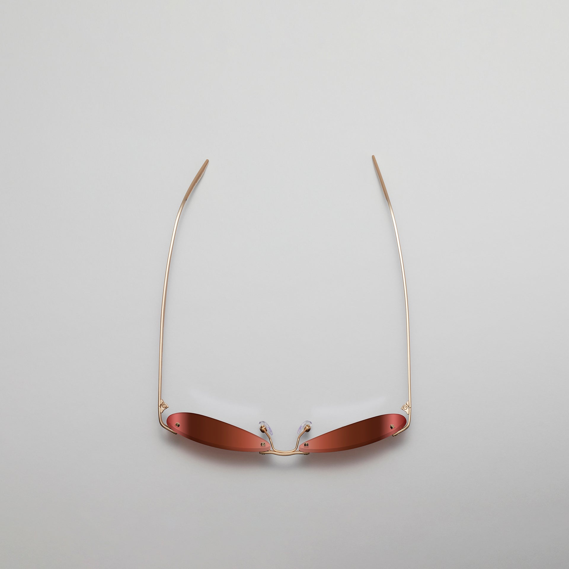 Sunglasses with gold frame and red lenses on a light gray background