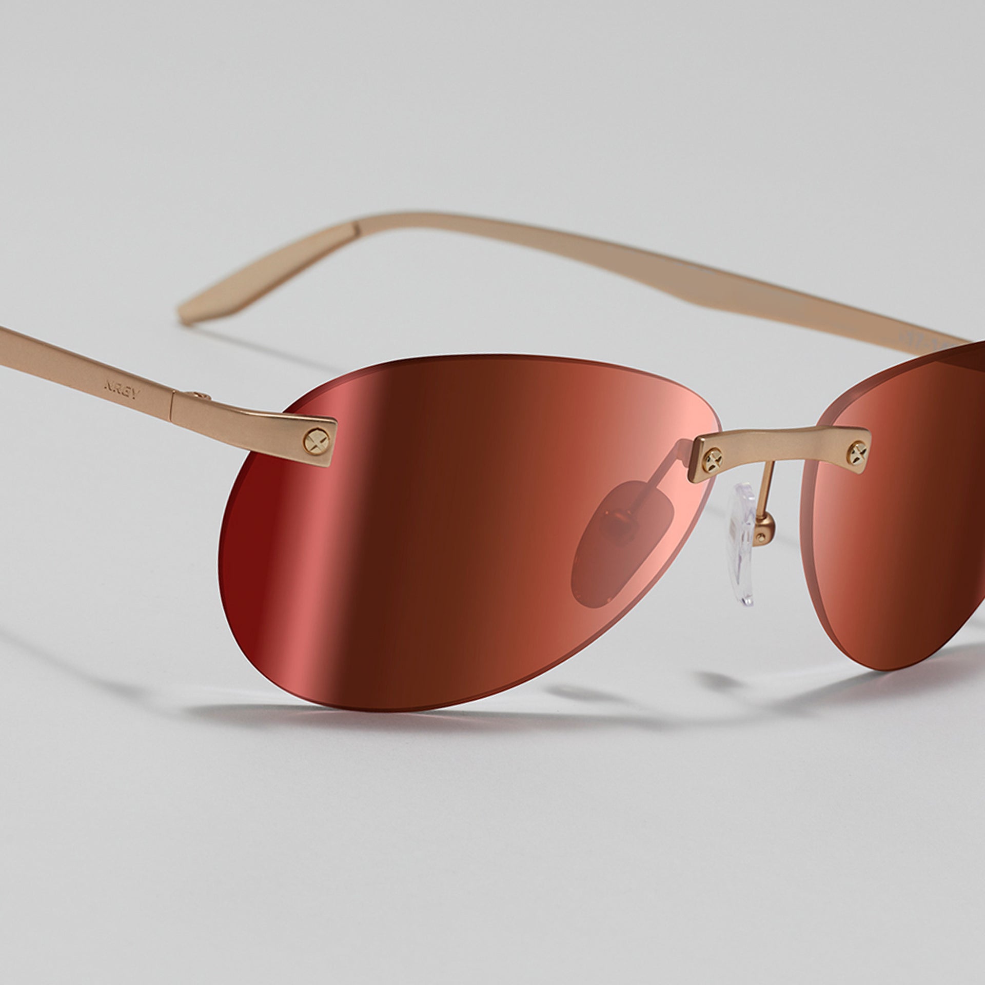 Sunglasses with red lenses and gold frames on a light gray background