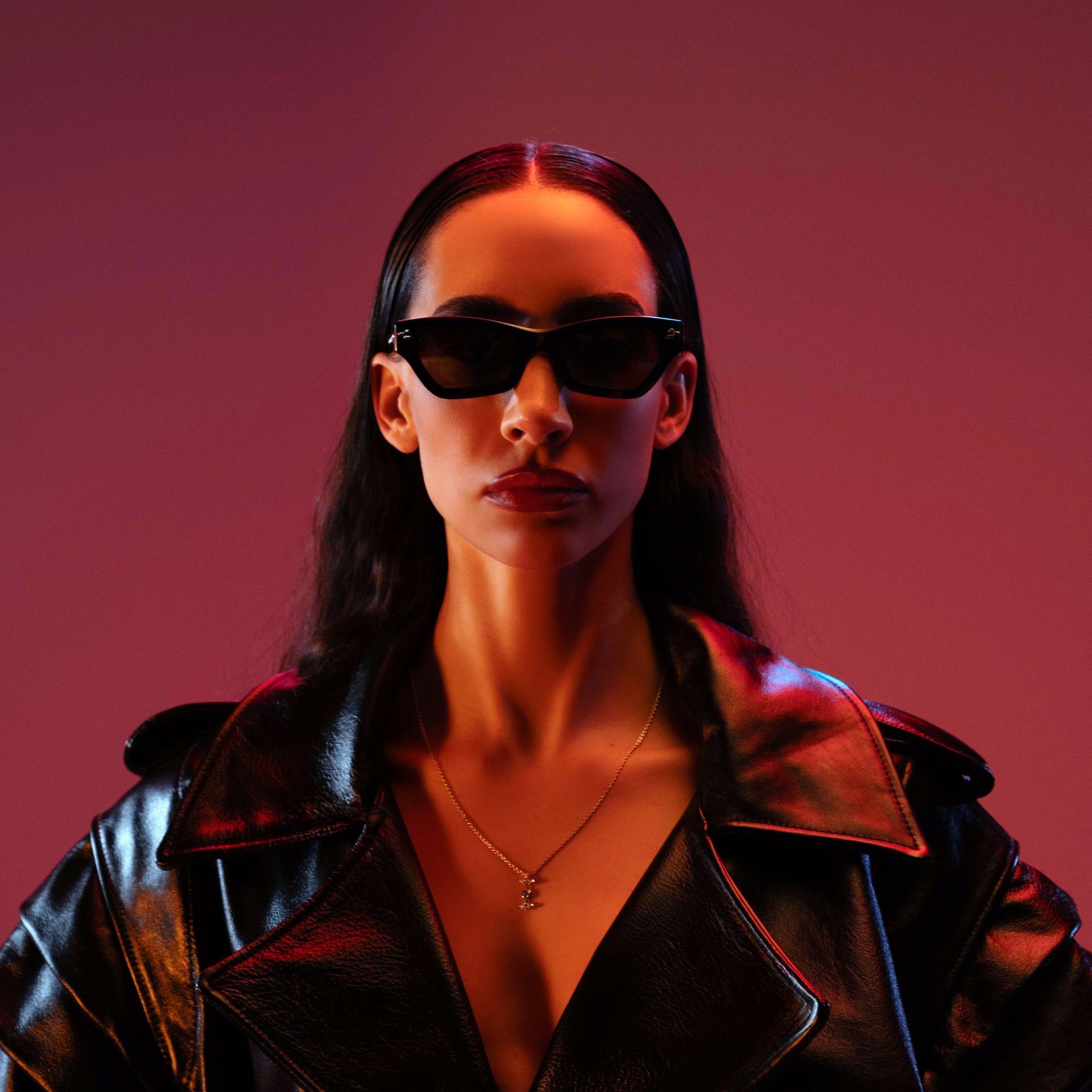 Person wearing a black leather jacket and sunglasses against a red background