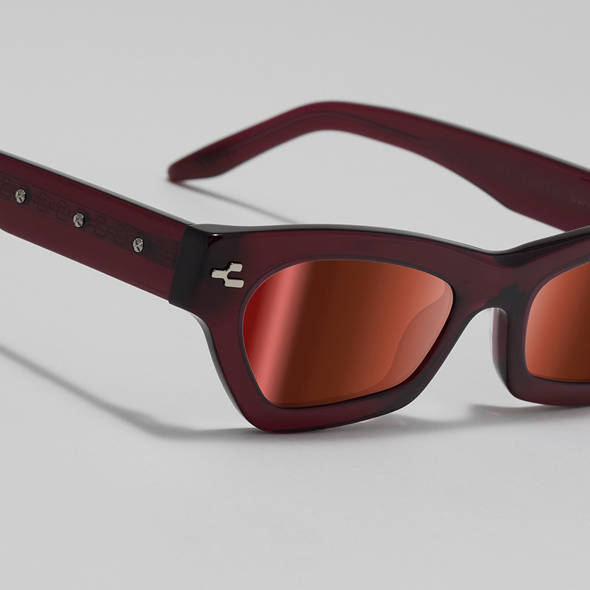 Sunglasses with maroon frame and red lenses on a light gray background