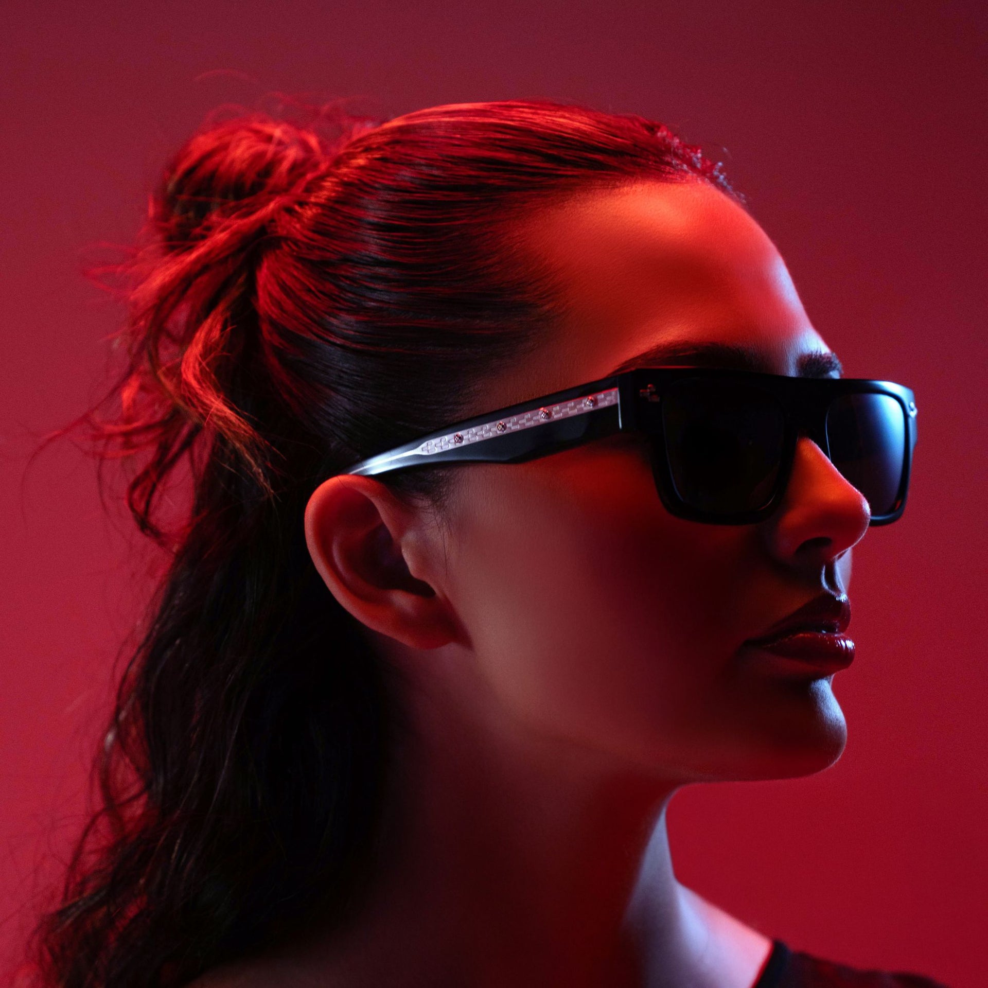 Woman wearing sunglasses with a red filter on a red background