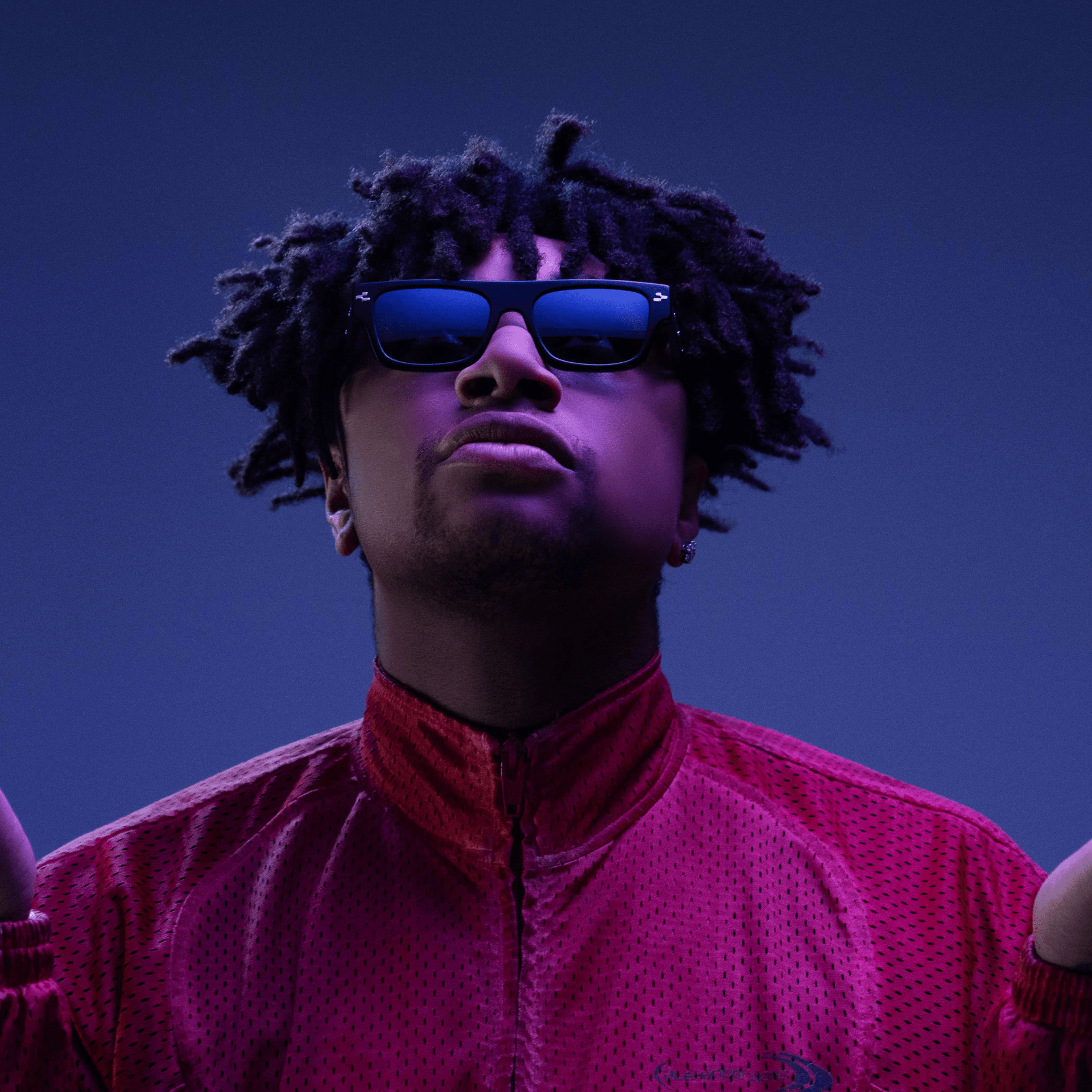 Person wearing sunglasses and a red jacket against a dark blue background