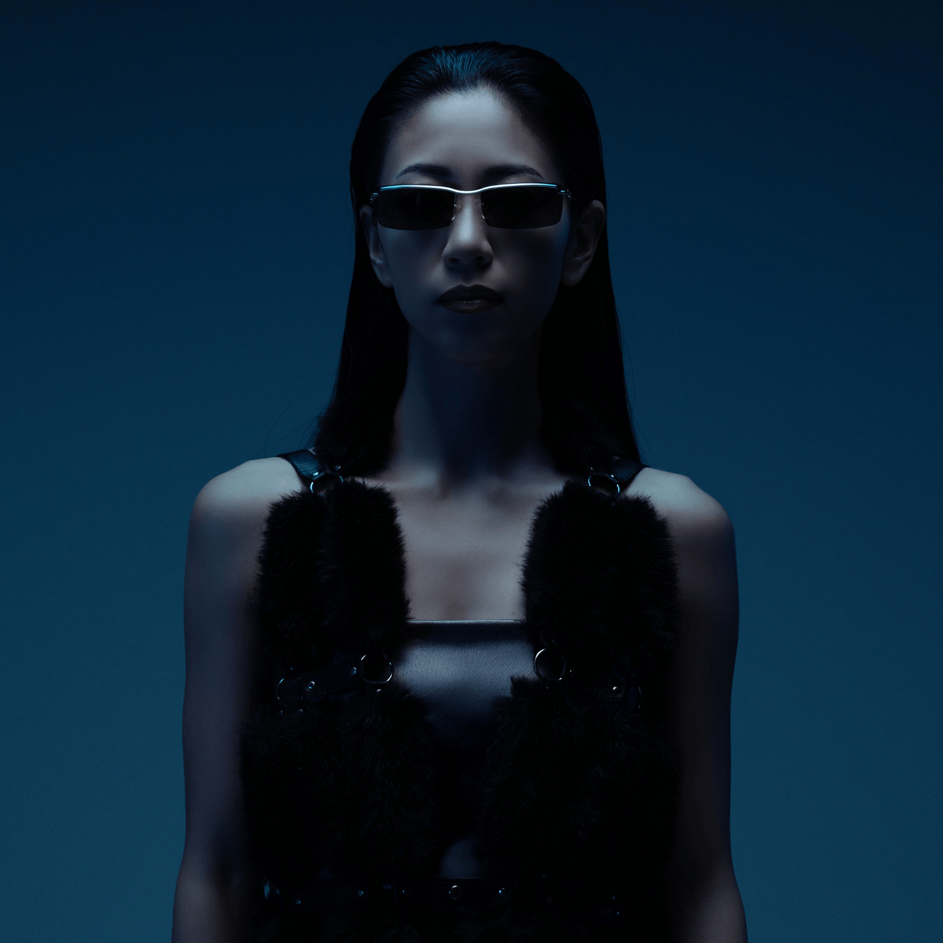 Person wearing sunglasses and a dark outfit against a blue background