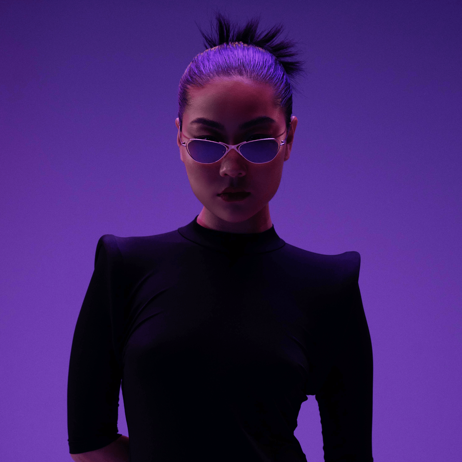 Person wearing a black outfit and purple sunglasses against a purple background