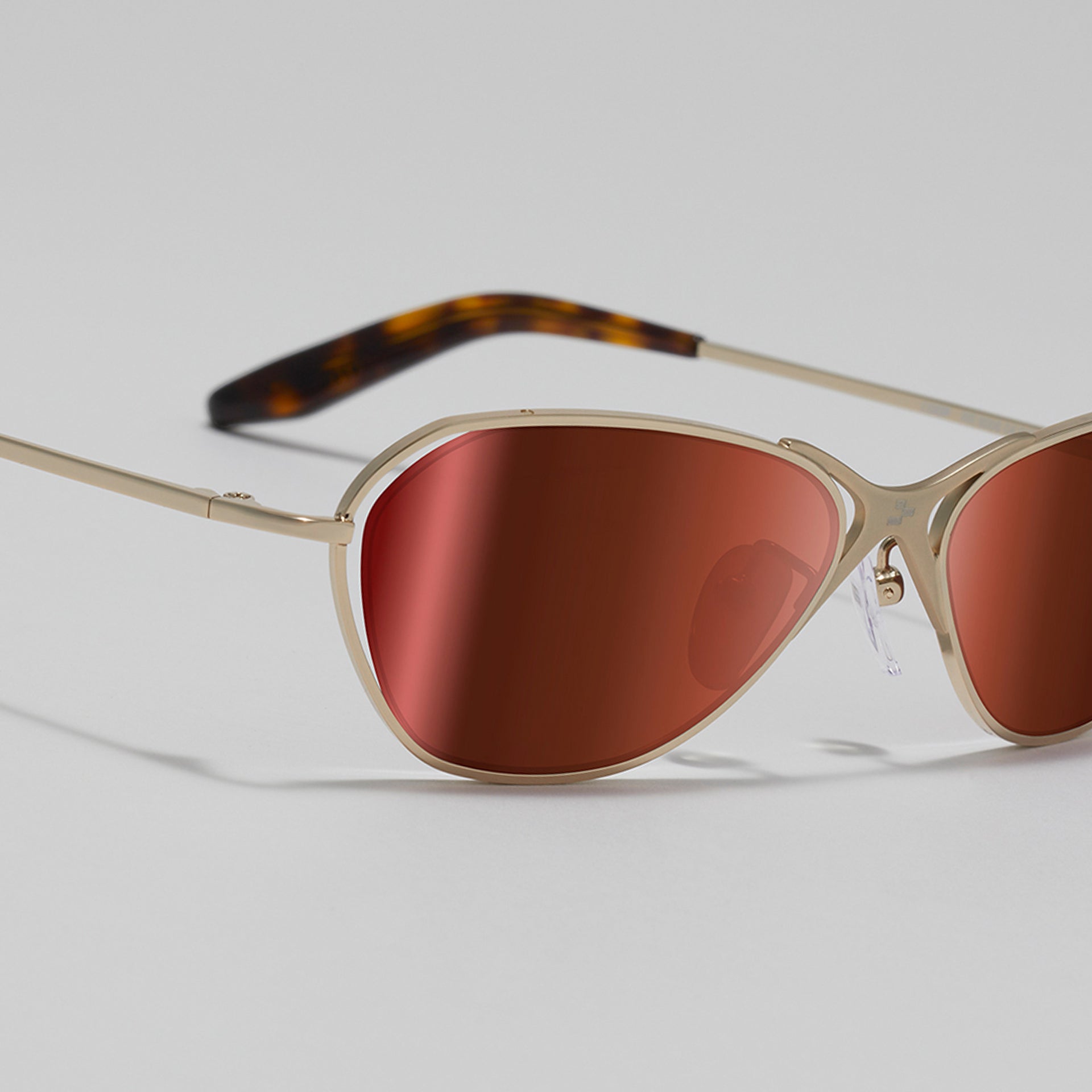 Sunglasses with red lenses and gold frame on a light gray background