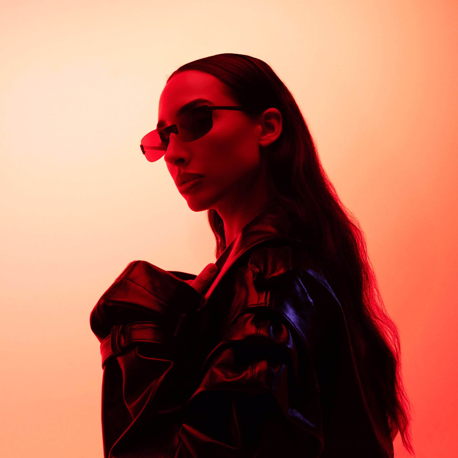 Person wearing sunglasses and a dark jacket against a red and orange gradient background