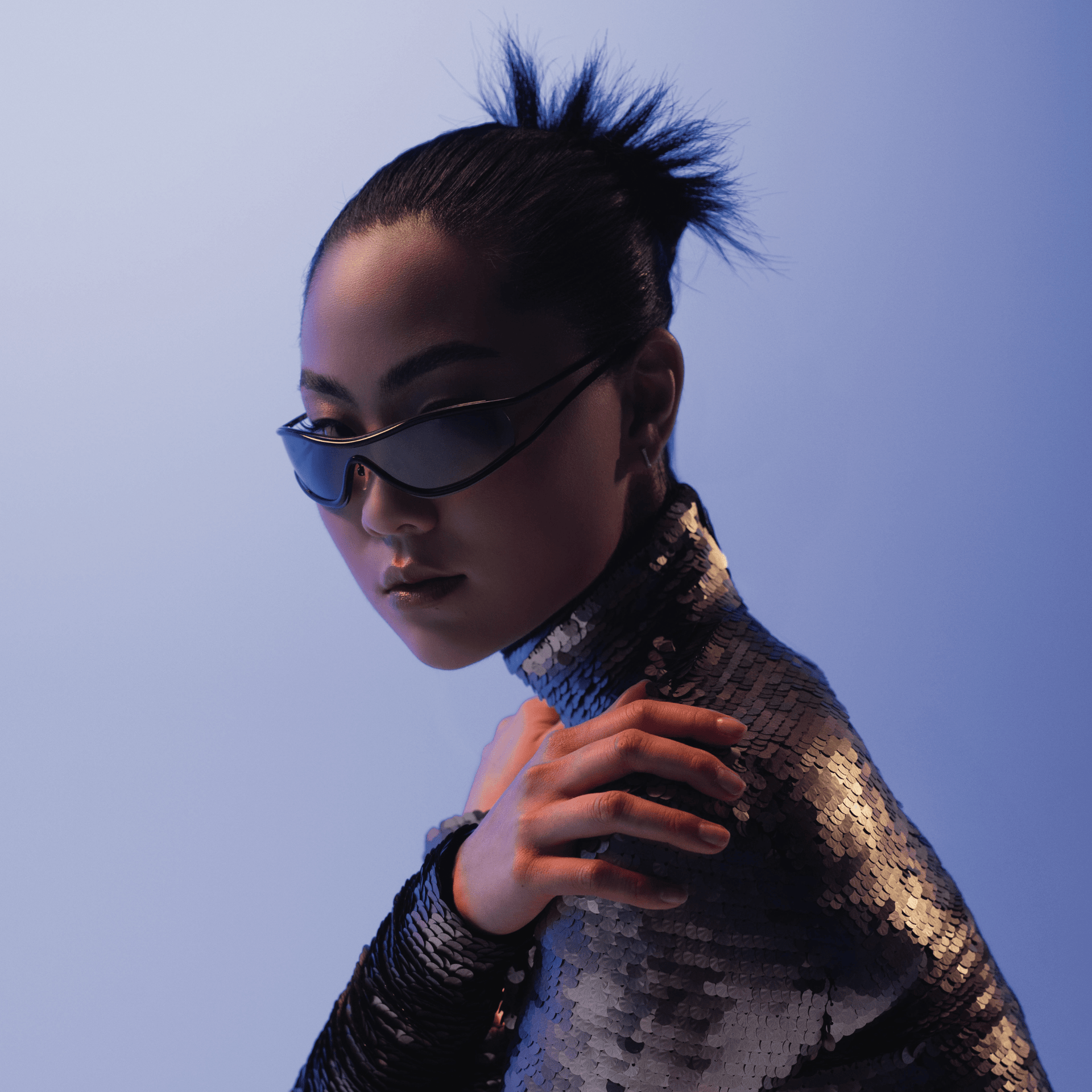 Person wearing futuristic sunglasses and a sequined outfit against a blue background