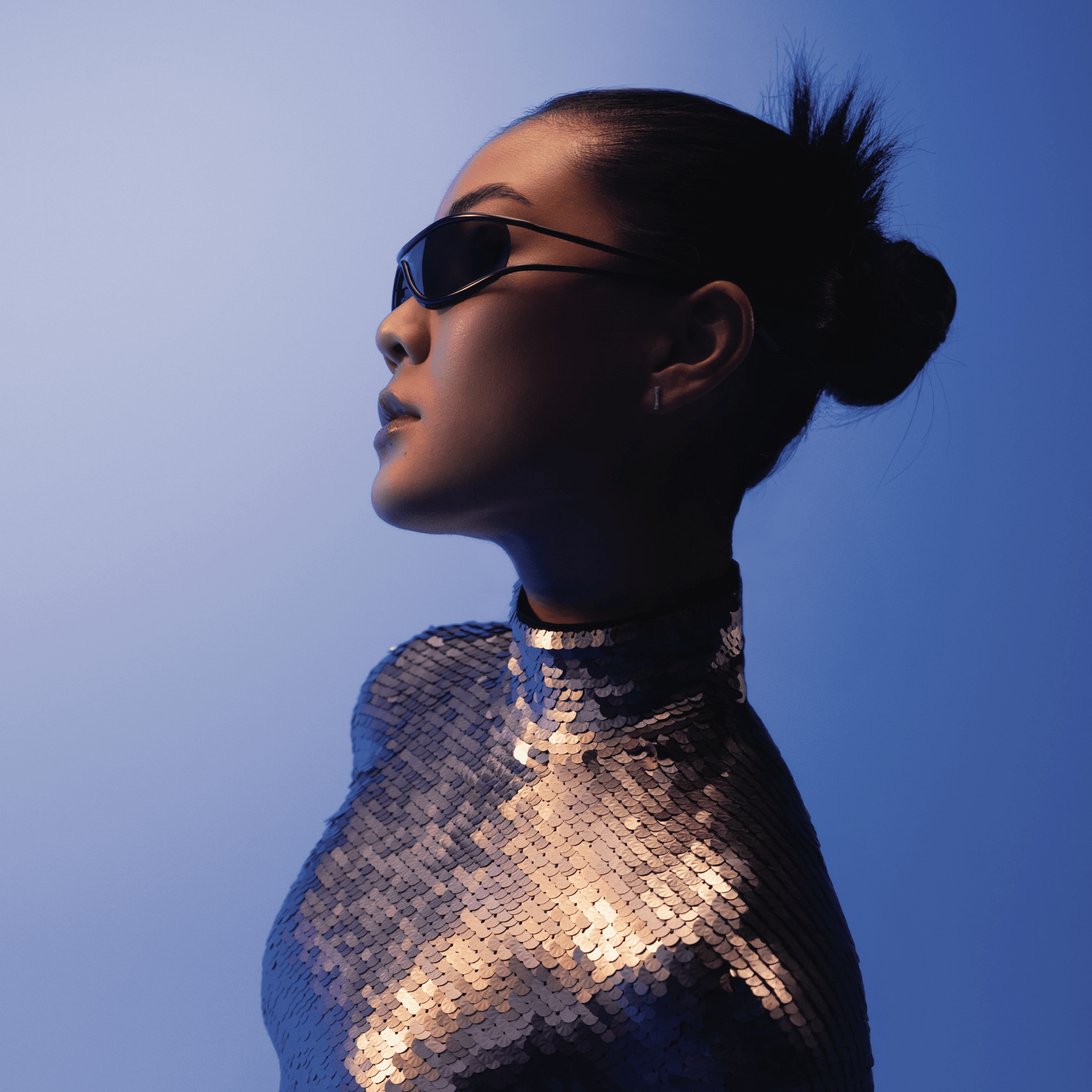 Person wearing a sequined outfit and sunglasses against a blue background