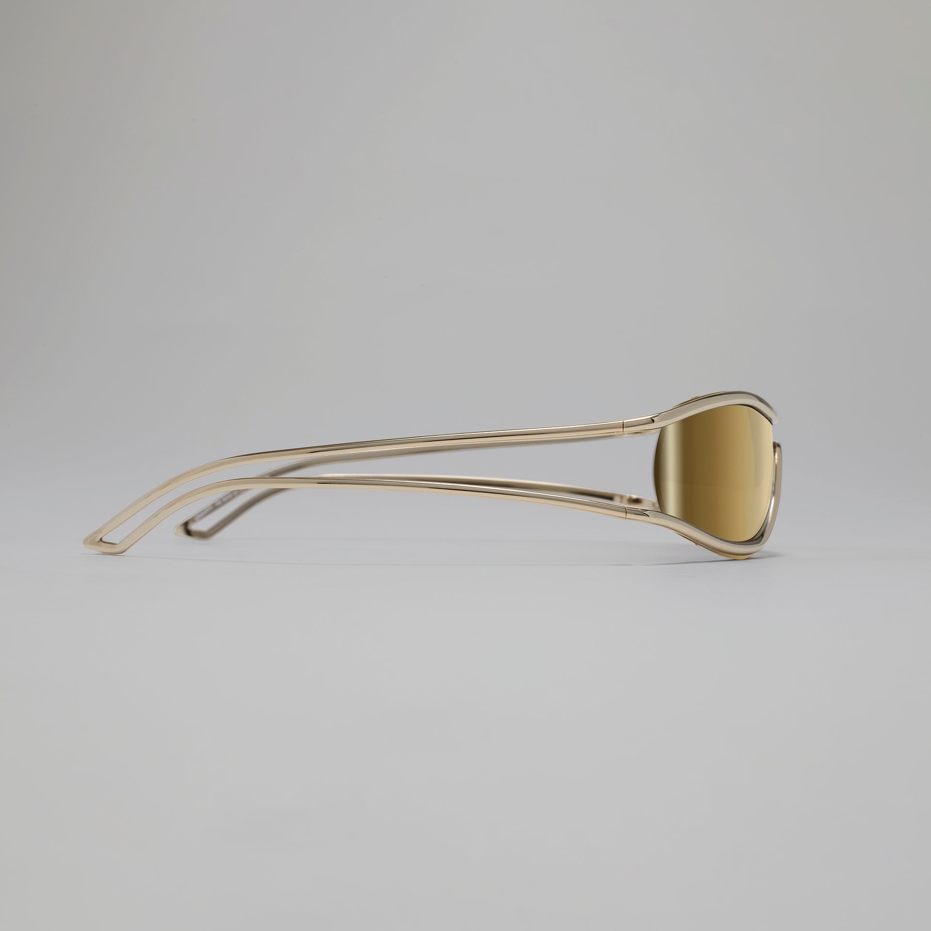 Gold-colored sunglasses on a light gray background