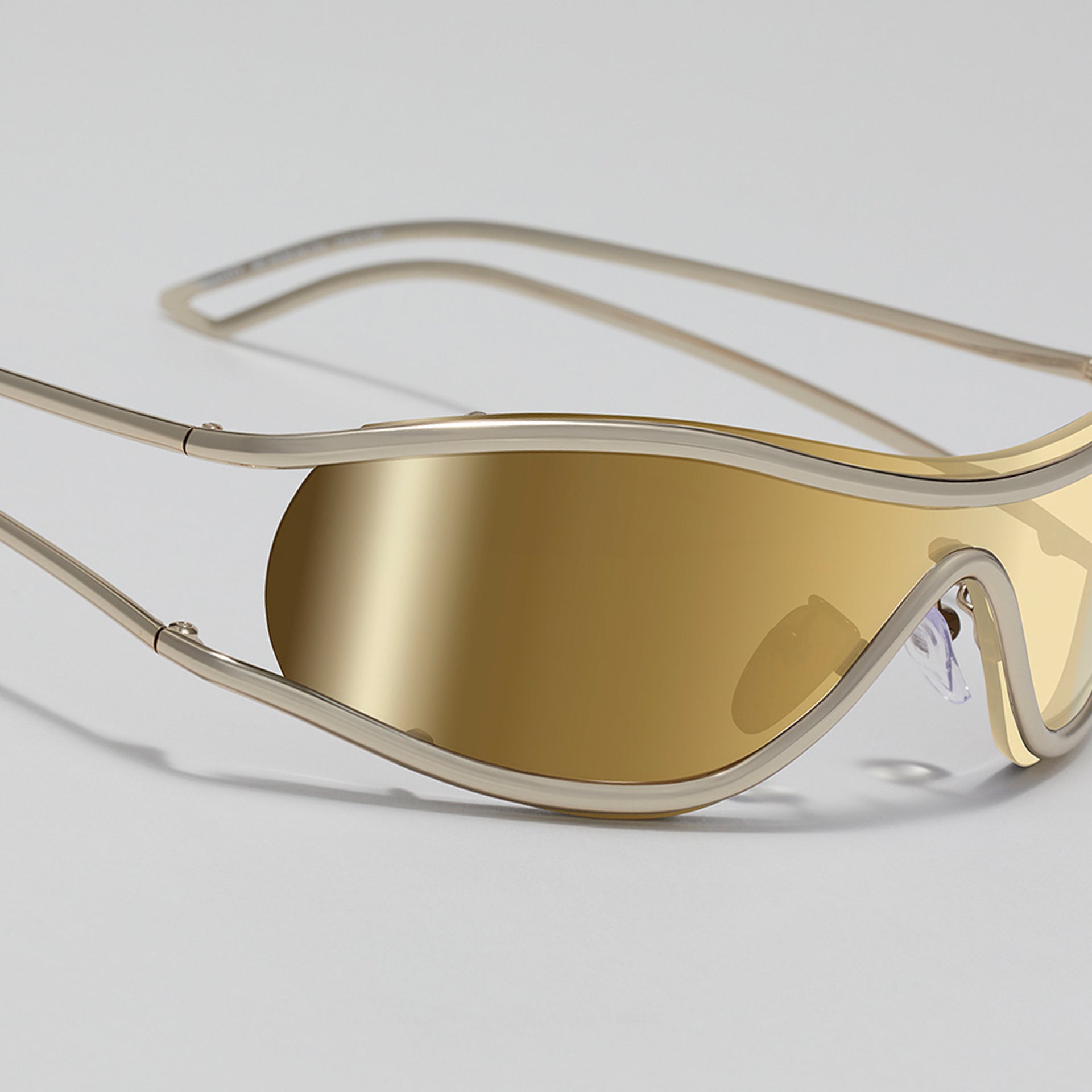 Gold sunglasses with a reflective lens on a light gray background