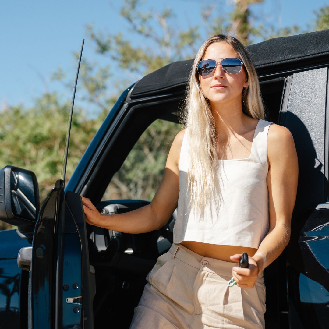 Woman standing next to a car outdoors wearing sunglasses and a sleeveless top.