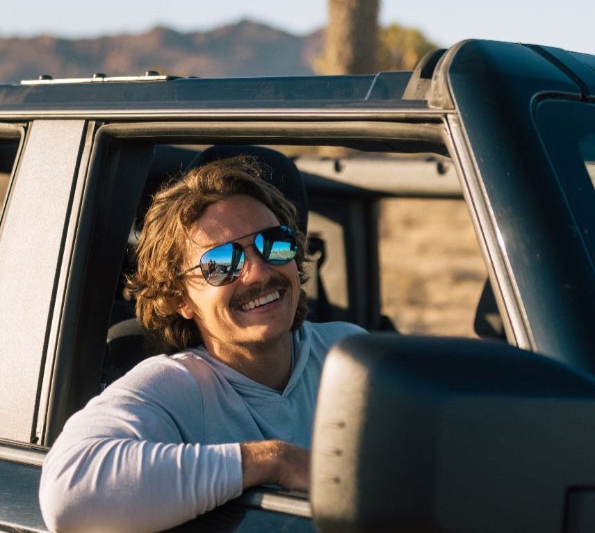 Man with sunglasses leaning out of a car window in a desert setting