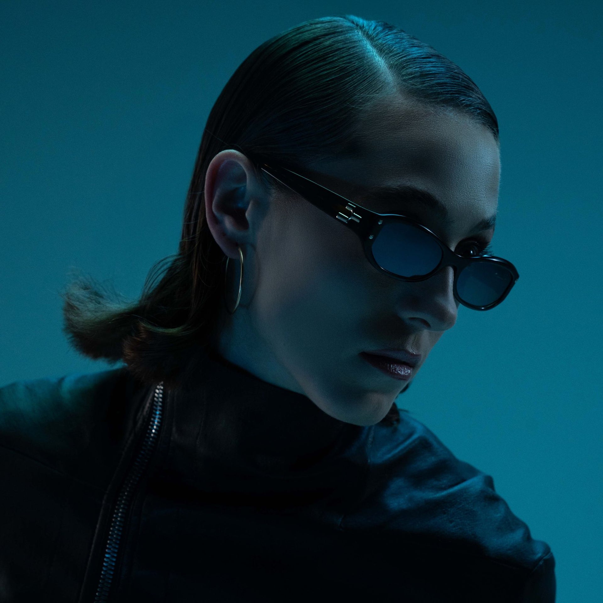 Person wearing sunglasses with a blue tint against a dark background