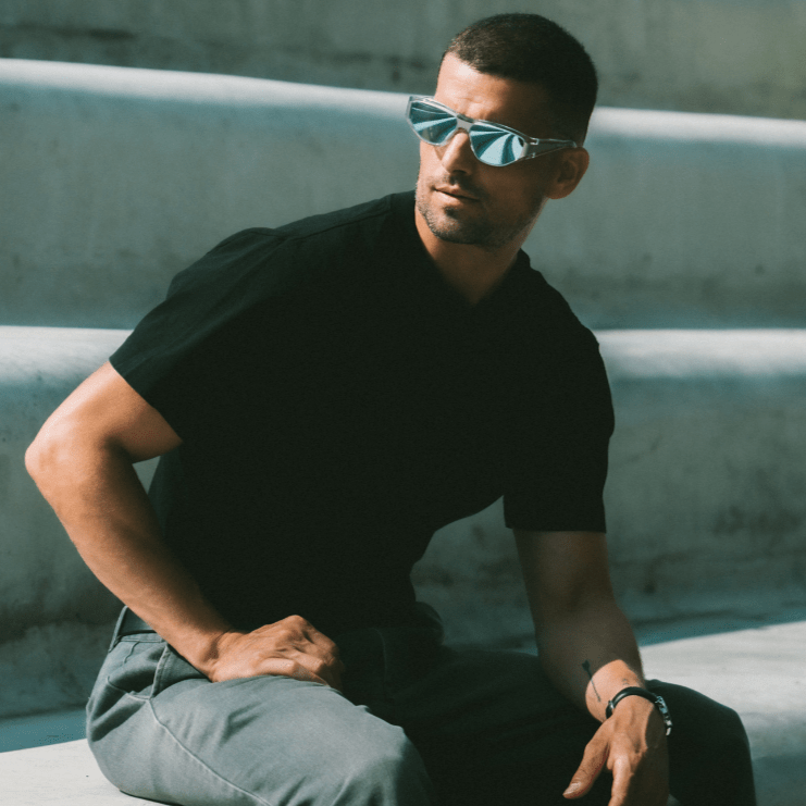 Man wearing sunglasses and a black shirt sitting on concrete steps.