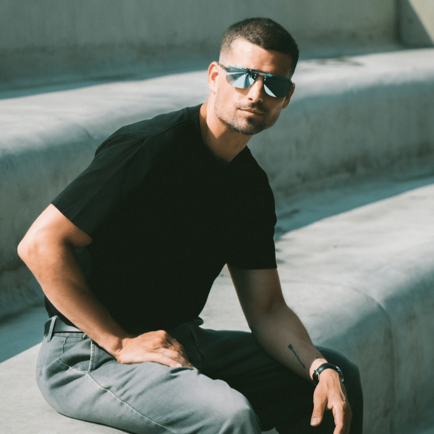 Man wearing sunglasses and a black shirt sitting on concrete steps.