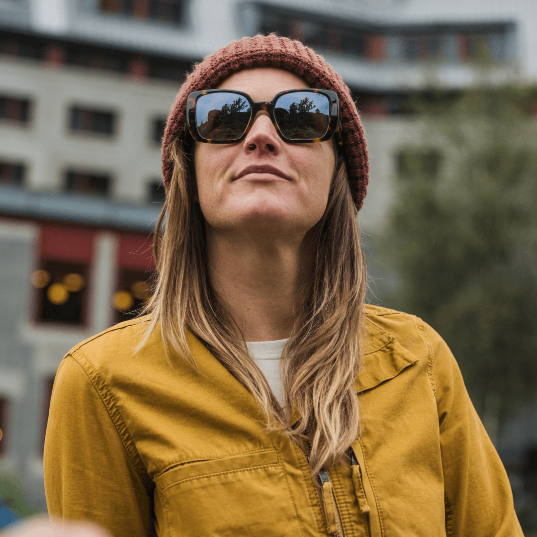 Person wearing sunglasses and a beanie with a blurred urban background