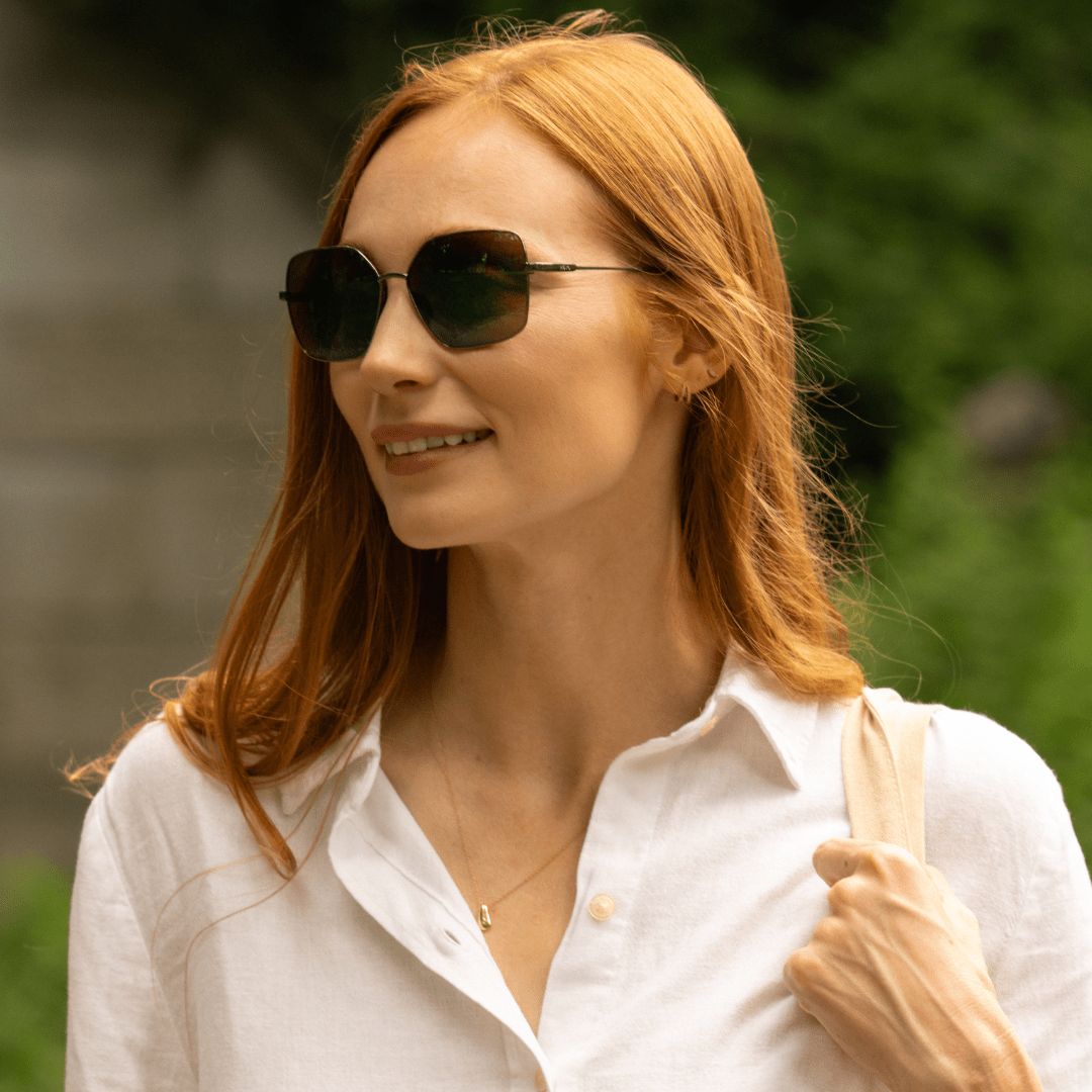 Side profile of a woman in a white shirt wearing Bella oversized metal sunglasses with dark lenses.