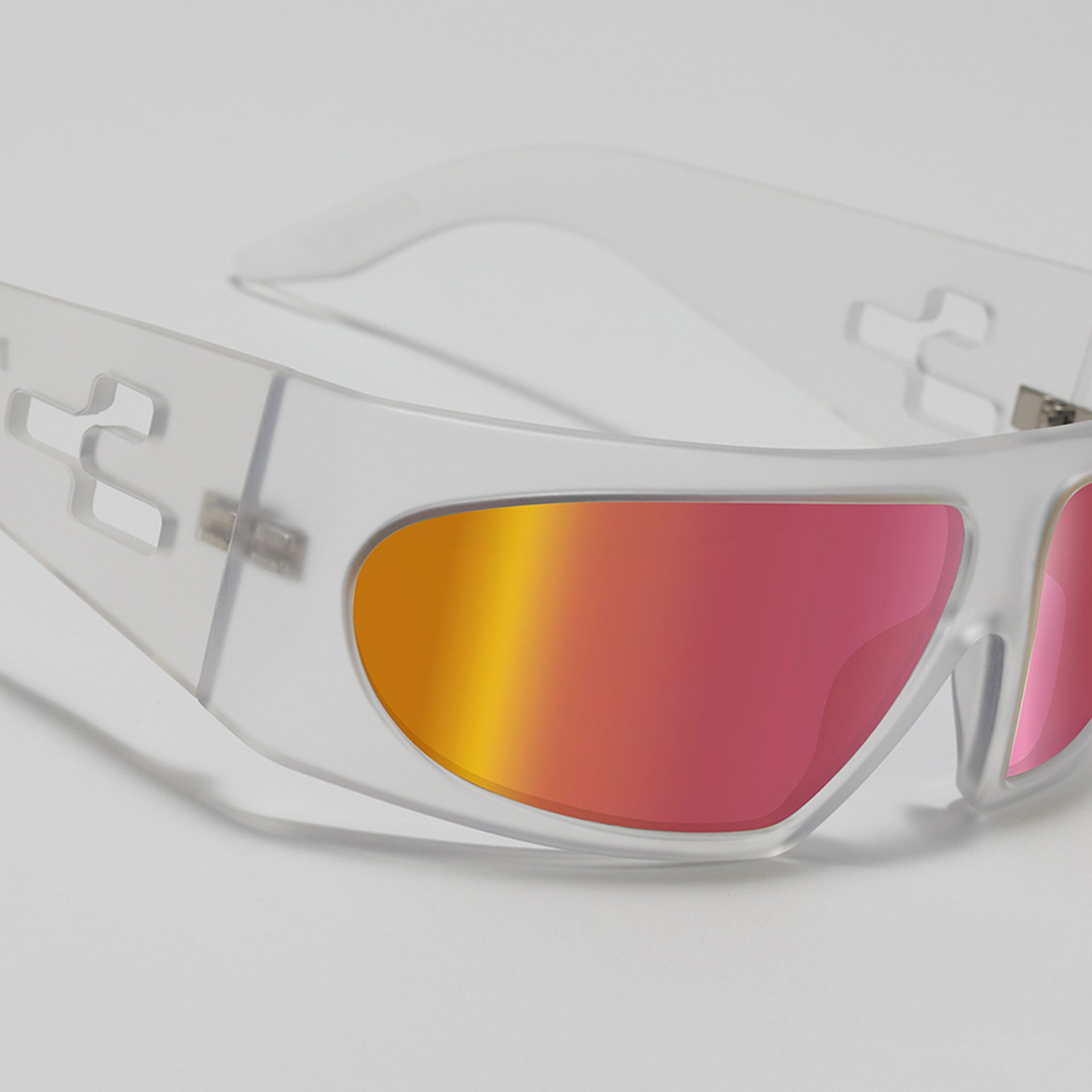Sunglasses with clear frame and red-orange reflective lenses on a light gray background