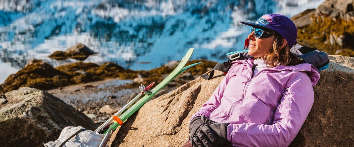Skier resting on a rock in the snow wearing Revo Traverse sunglasses with Blue Water lenses
