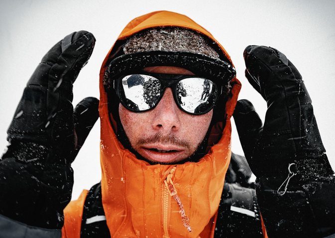 Snowboarder in an orange jacket wearing Revo glacier glasses